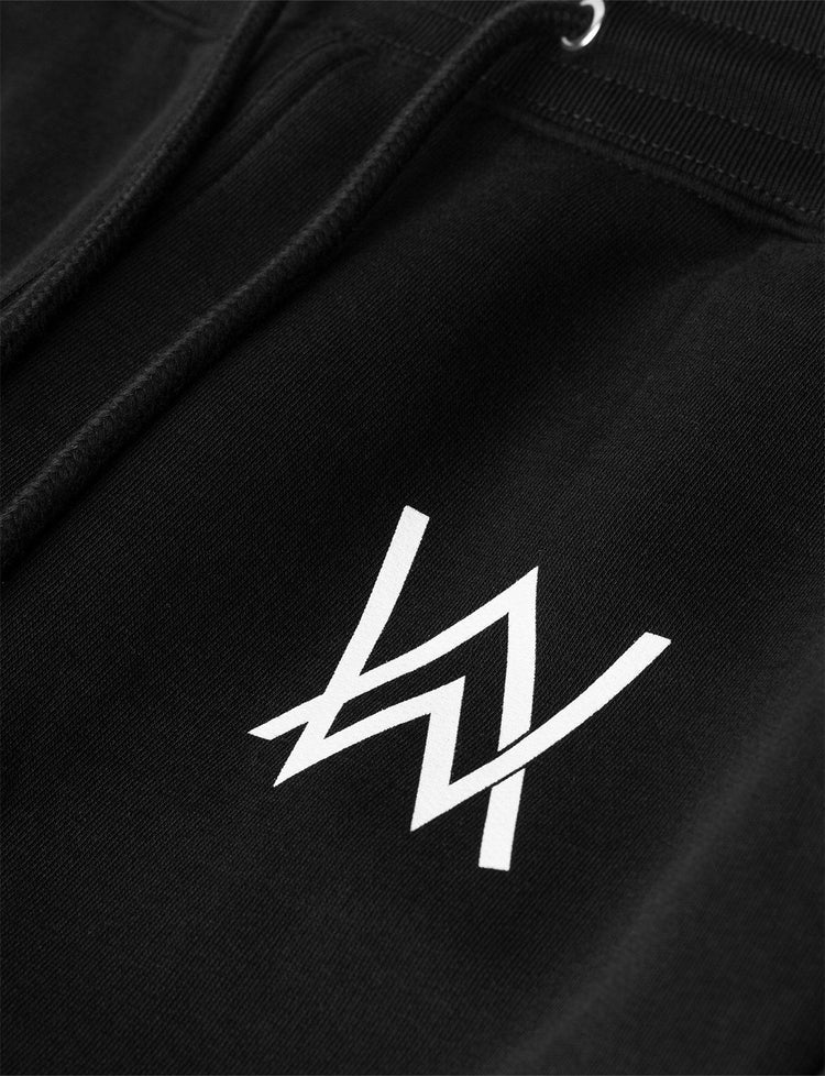 Detail of the Alan Walker Core Drone Sweatpants featuring the iconic 'AW' logo in white on the front left side, emphasizing the brand's signature style on a black fabric background.