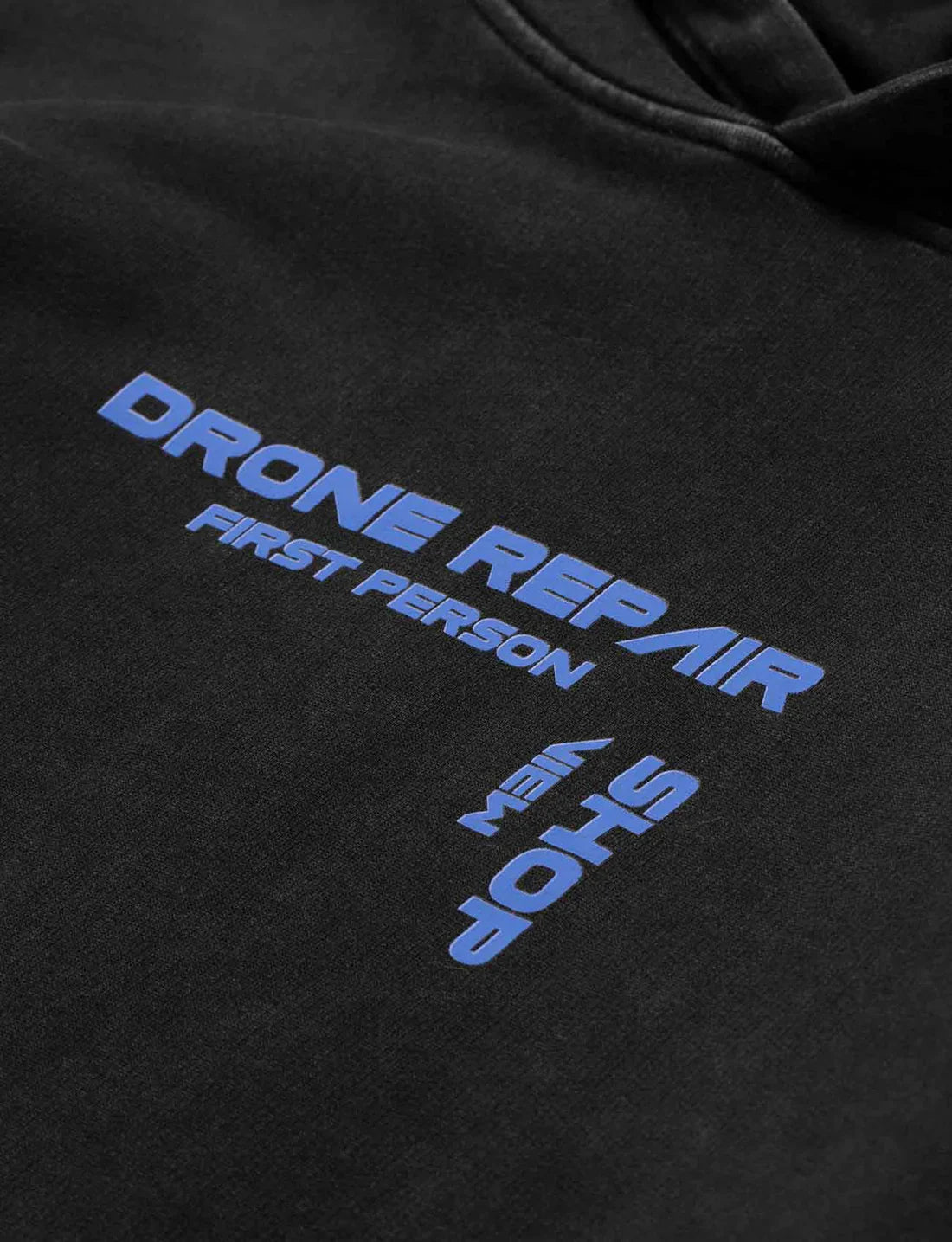 Zoomed-in view of the Drone Repair Shop Hoodie's chest area, displaying the blue 'DRONE REPAIR FIRST PERSON SHOP' text, emphasizing the specialized theme of the hoodie.
