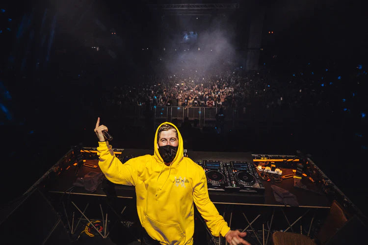 Alan Walker in iconic Yellow Hoodie onstage at a packed music event.