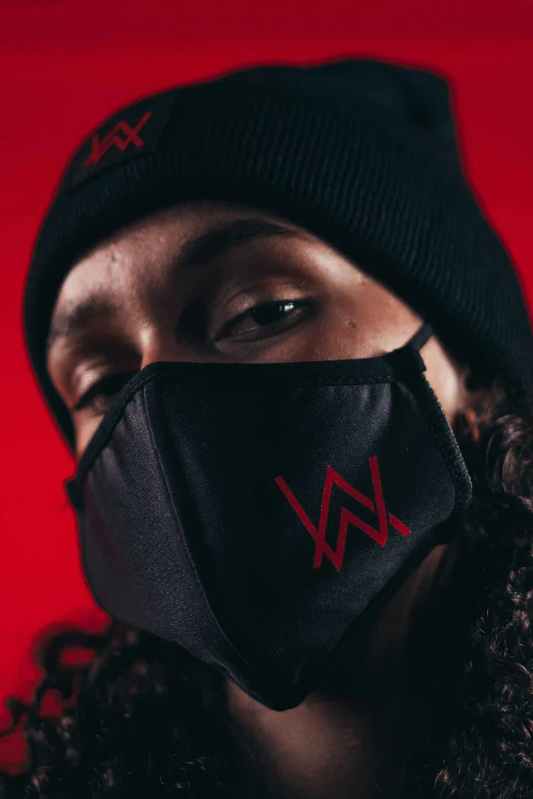 Portrait of a curly-haired individual with a black knit cap and matching Alan Walker mask with a distinctive red logo.