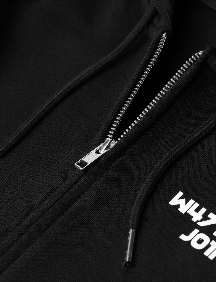 Detailed view of the CORE LOGO ZIP HOODIE's high-quality zipper and 'W4LK3RS JOIN' logo, emphasizing the garment's fine craftsmanship and durable design, set against a textured black fabric background.