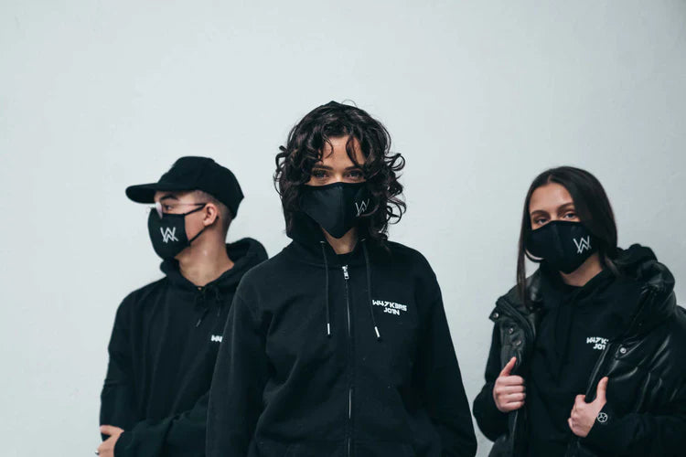 Trio wearing Alan Walker's CORE LOGO ZIP HOODIE and face masks, each emblazoned with the AW logo, standing confidently against a minimalist backdrop, representing unity in style and urban fashion.