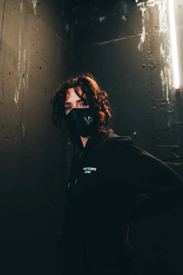 Mysterious figure in an urban setting wearing the CORE LOGO ZIP HOODIE and matching mask, both adorned with the 'AW' logo, creating a cohesive and stylish streetwear ensemble.