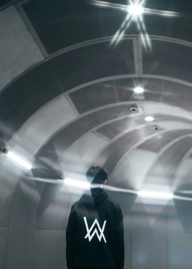 Silhouetted figure standing in a contemporary tunnel, backlit by soft lighting, wearing the CORE LOGO ZIP HOODIE with a prominent 'AW' logo, symbolizing urban exploration and modern lifestyle.