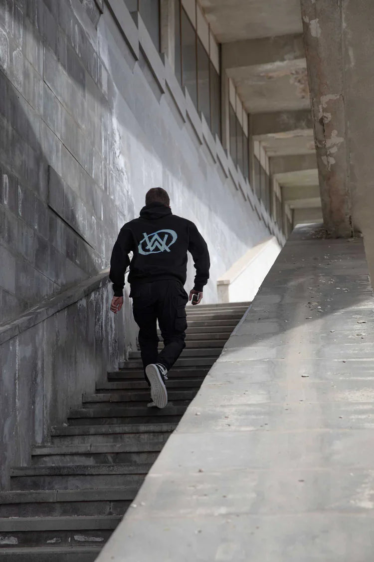 Urban exploration with a touch of fan pride, a person in an Alan Walker hoodie ascending concrete stairs, back to the camera.