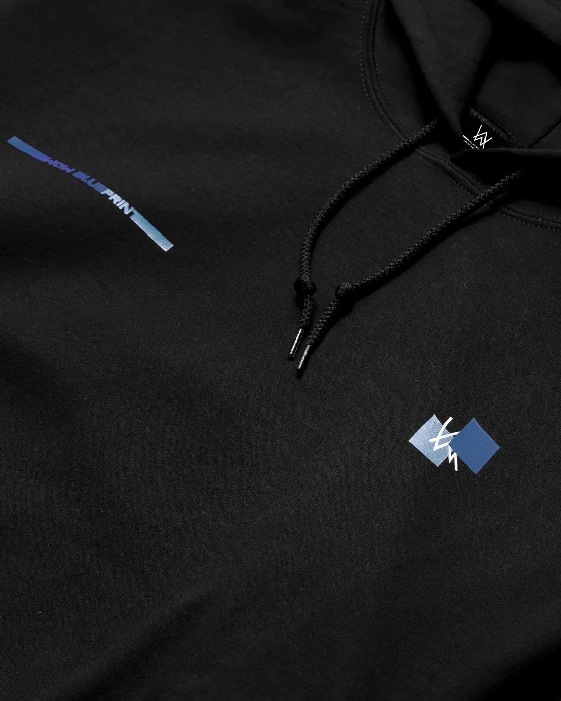 Close-up view of Alan Walker Blueprint Hoodie detailing with blue graphic text and logo on black fabric, showcasing quality stitching and hood drawstrings.