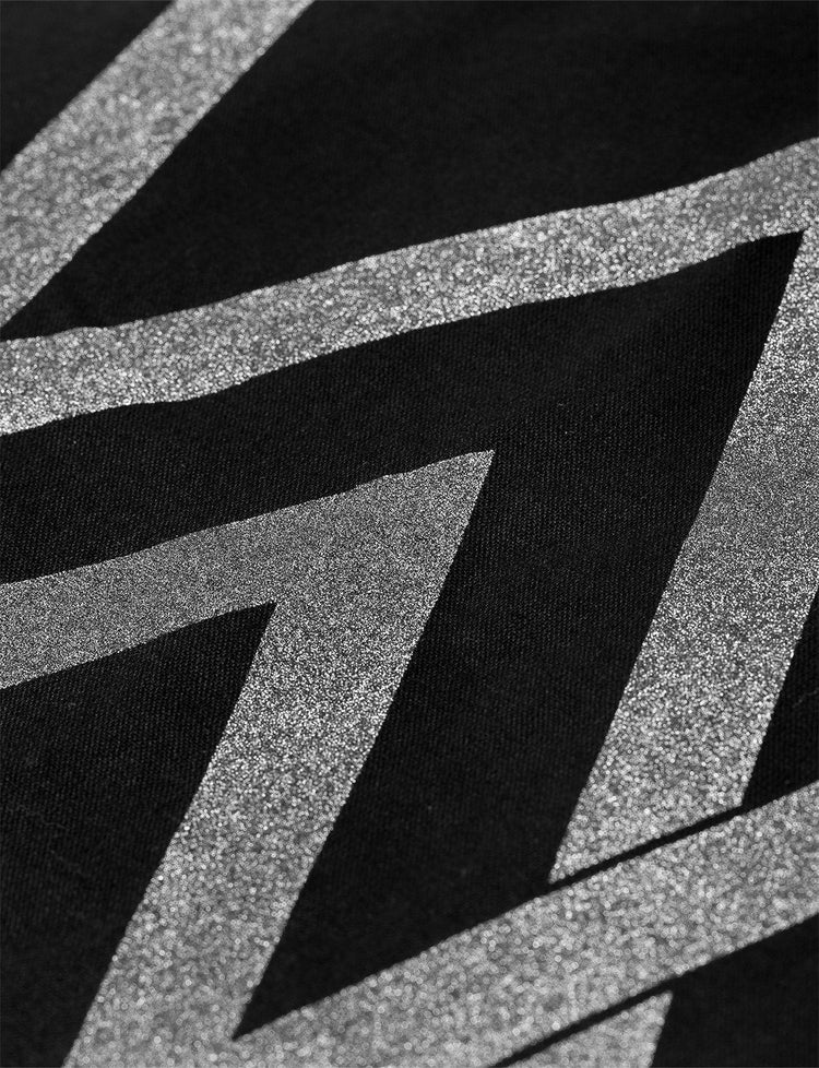 Macro shot of the CORE REFLECTIVE TOTE BAG's shimmering 'AW' logo, highlighting the reflective detail against the black canvas, illustrating the bag's stylish functionality.