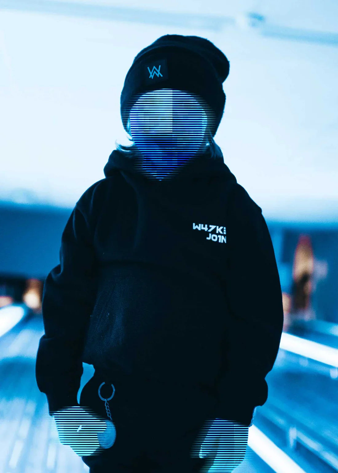 Back view of a child wearing the Alan Walker hoodie, looking at a DJ set, symbolizing a future in music.