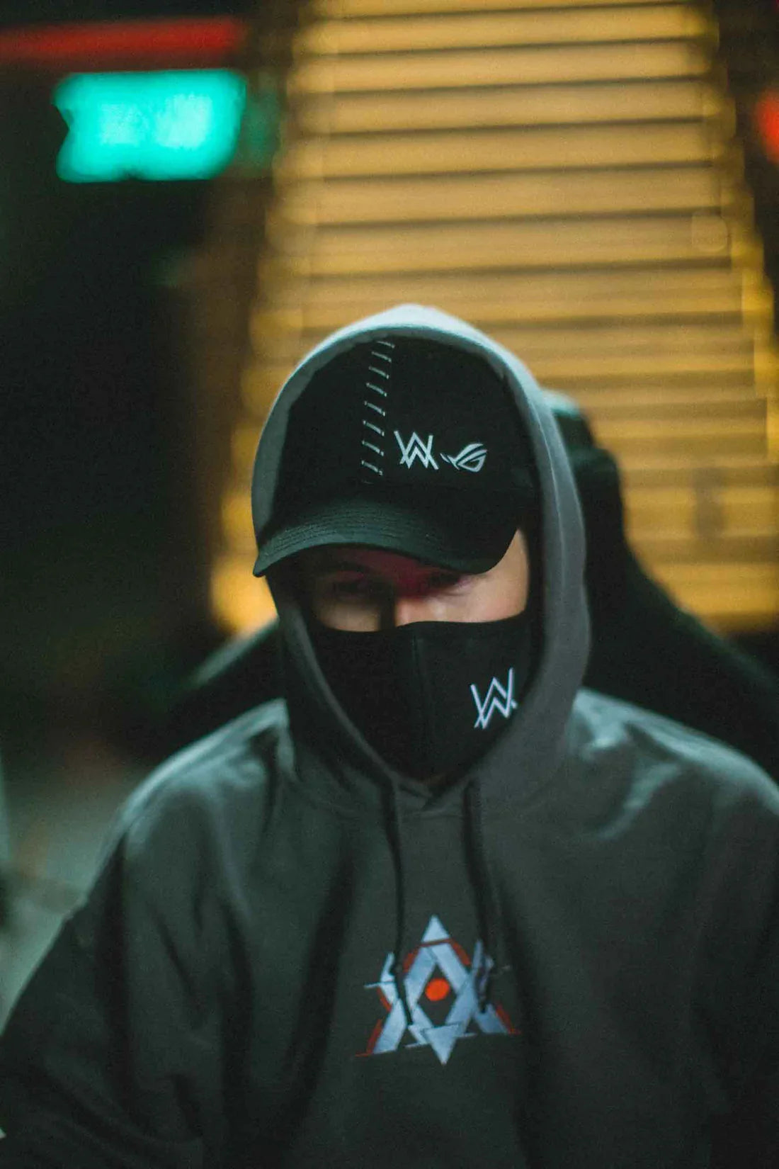 Mysterious figure in a gray Alan Walker Gaming Hoodie and black cap, blending into the urban night, a subtle nod to gamer street fashion.