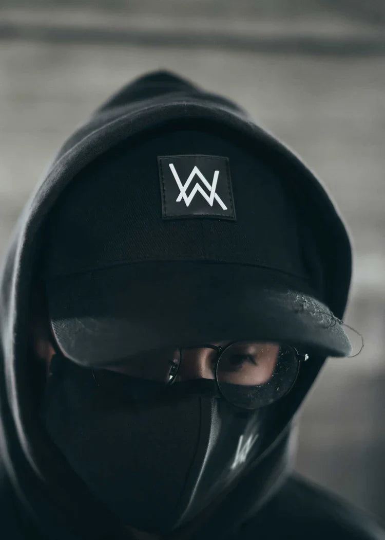 Stylized portrait of an individual wearing the Alan Walker Core Logo Cap, featuring the prominent 'AW' logo, paired with a matching black hoodie and mask, creating a mysterious and unified aesthetic.